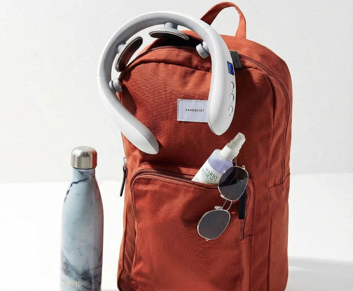 Red backpack with a water bottle, sunglasses, and other items on a white background